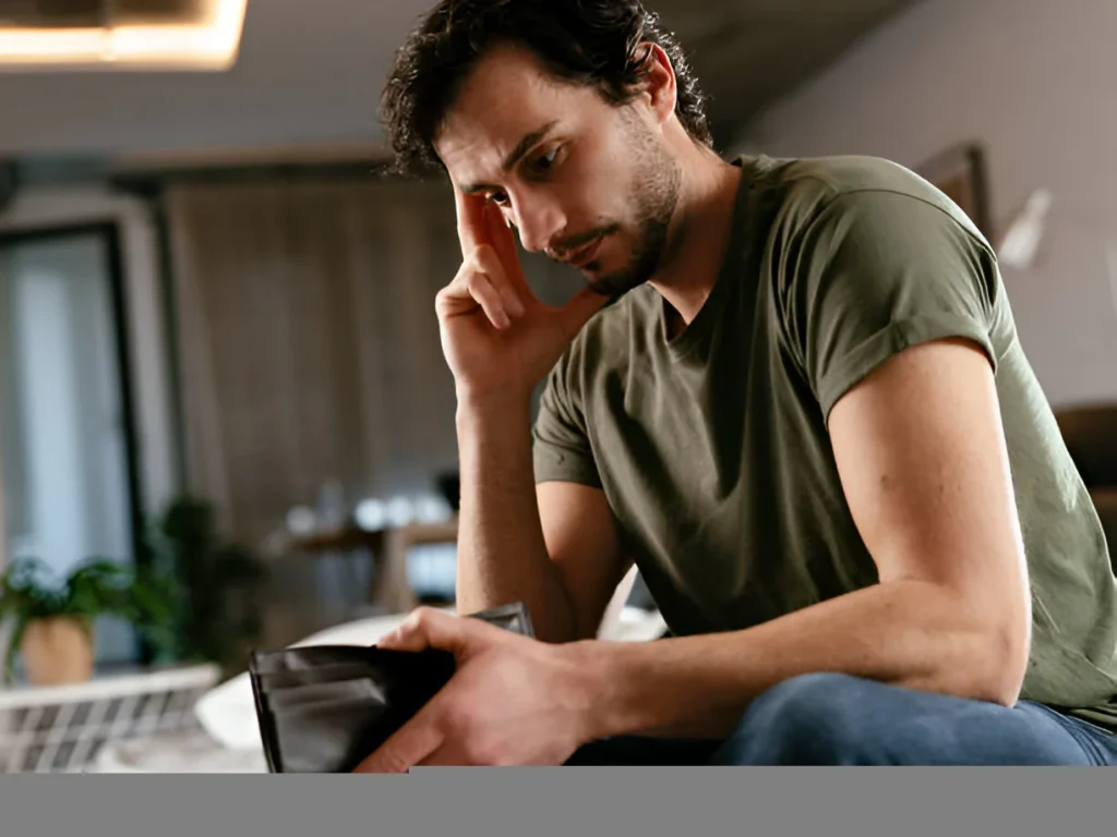 A sad man sitting at home looking at an empty wallet after loosing money in a drive Social Media Pyramid Scheme