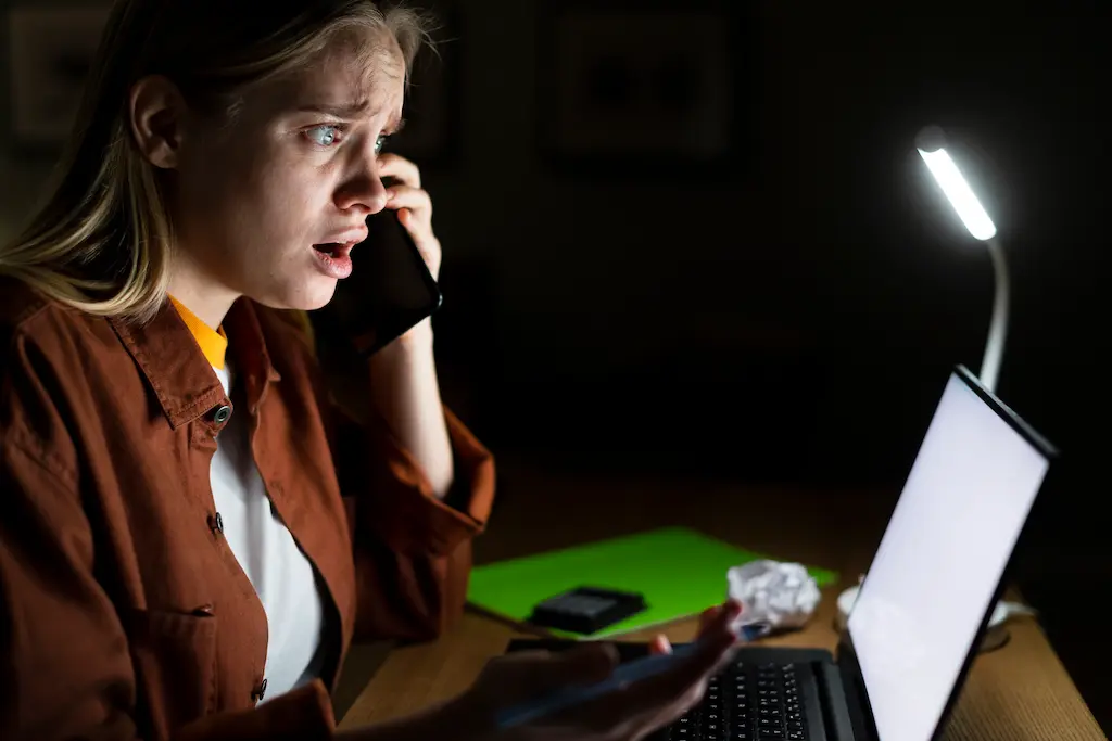 A worried individual speaking on the phone with a bank representative to report unauthorized or fraudulent charges.